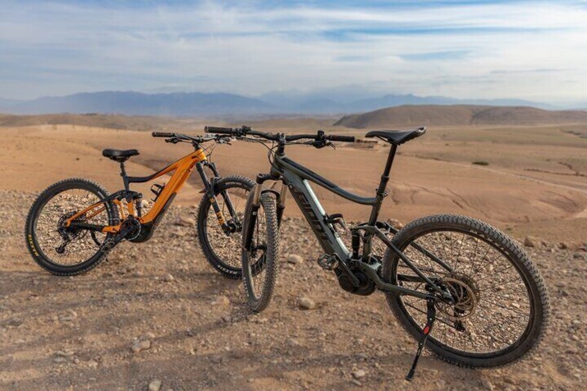 Deux vélos sont garés sur un terrain rocailleux, avec un paysage désertique en arrière-plan. 2