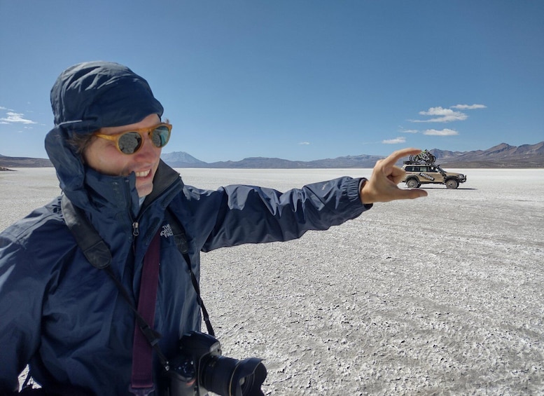 A person pointing at a vehicle in a barren landscape with mountains in the background. 2