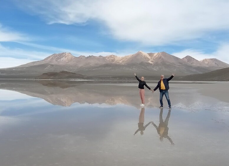 Two people holding hands on a reflective surface with mountains in the background. 3
