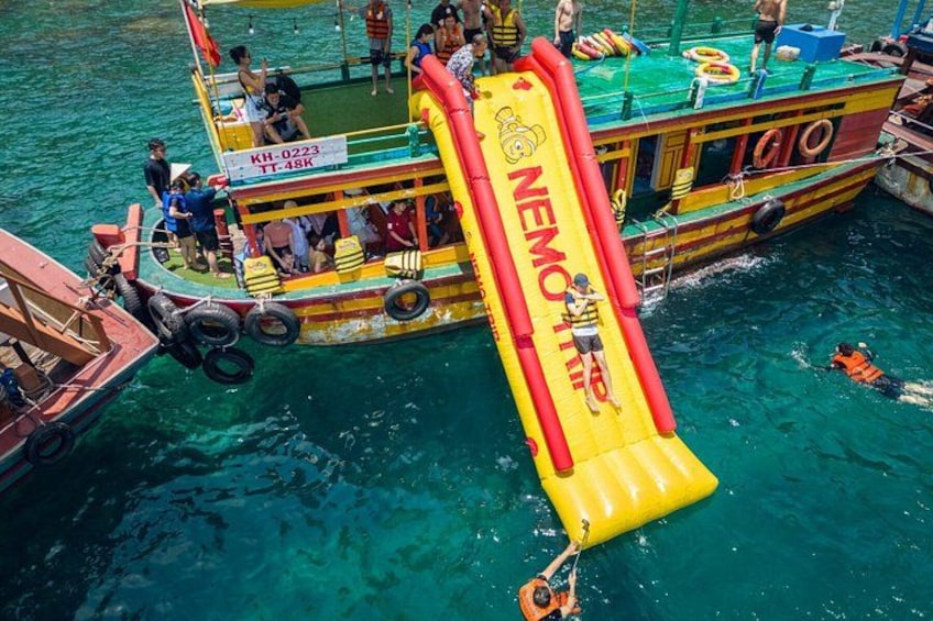 A colorful boat with a yellow inflatable slide, people on board, and clear blue water. 3
