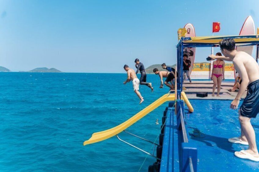 Een groep mensen op een boot met een gele glijbaan, die zich klaarmaakt om in het water te springen. 2