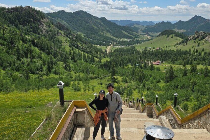 A man and a woman standing on a stone staircase with a view of a mountainous landscape. 1