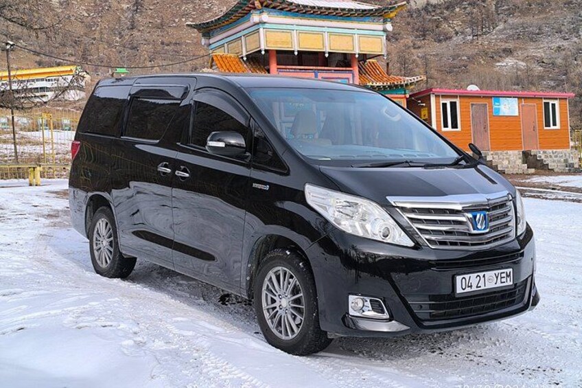 A black minivan parked on a snowy surface with a traditional building in the background. 2