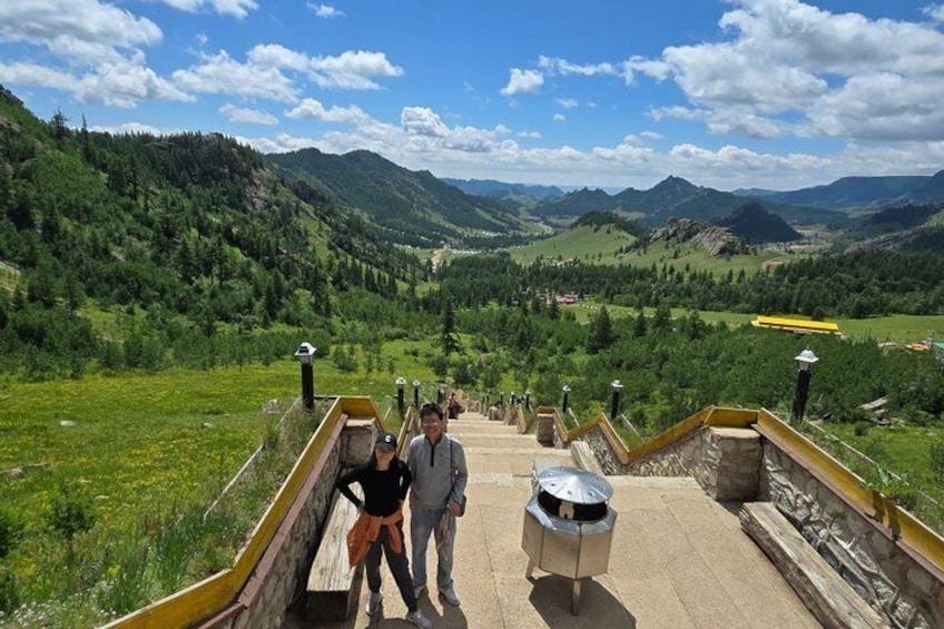 A paved pathway with a railing, a person standing, and a mountain landscape in the background. 4