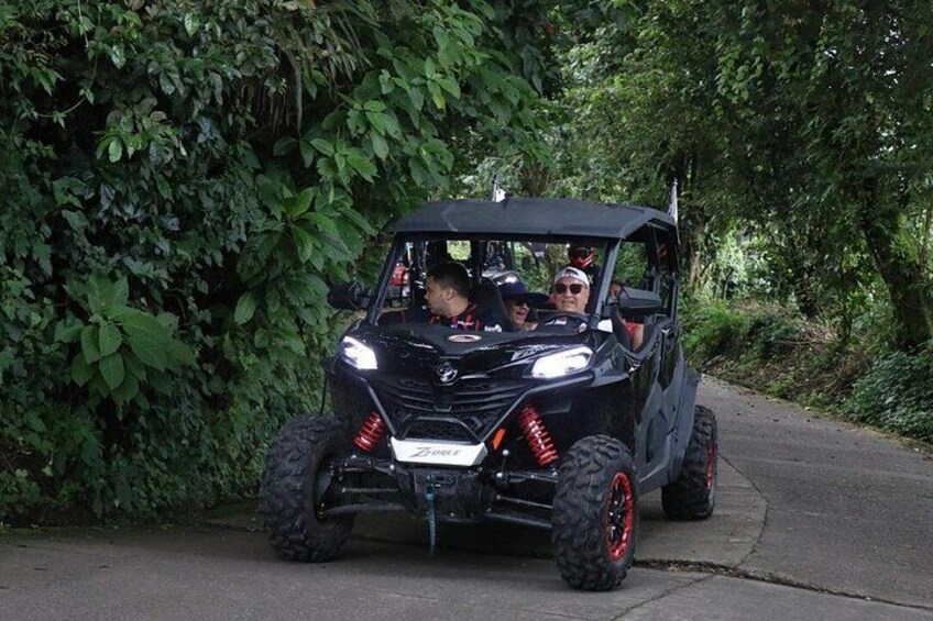 A black off-road vehicle with red accents driving on a paved road surrounded by dense greenery. 2