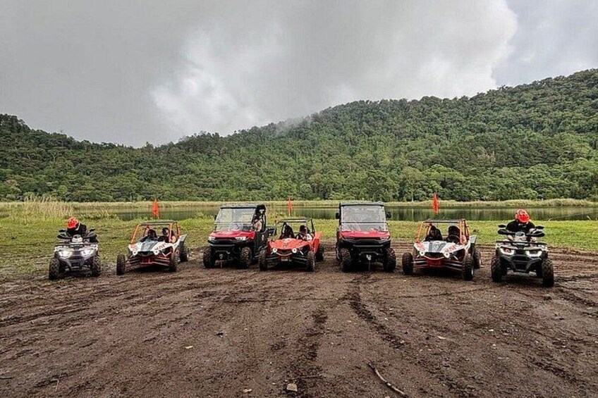 A group of off-road vehicles parked on a dirt road with a forested hill in the background. 3