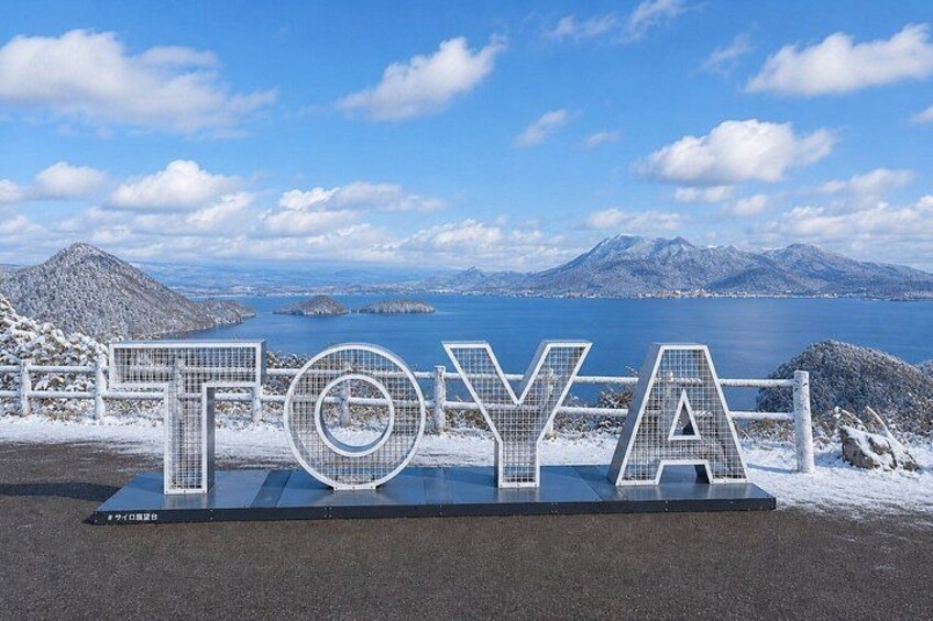A sign with the word 'TOYA' in large letters, a snowy landscape, and a body of water with mountains in the background. 4