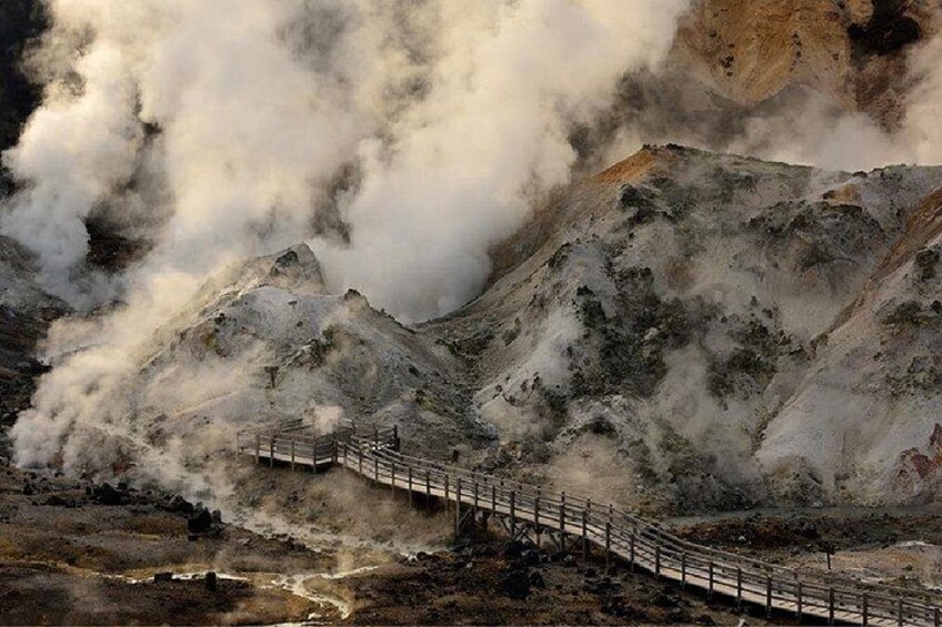 A wooden walkway leading up a mountain with steam rising from the ground. 1