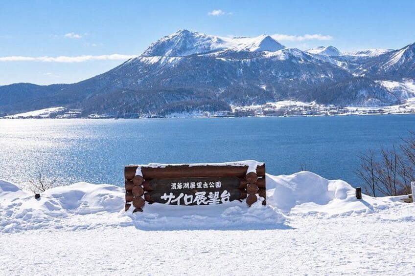 A wooden bench with Japanese text in a snowy landscape with a lake and mountains in the background. 3
