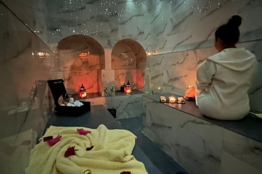 A person sitting by a wall with candles, a blanket, and a box. 1