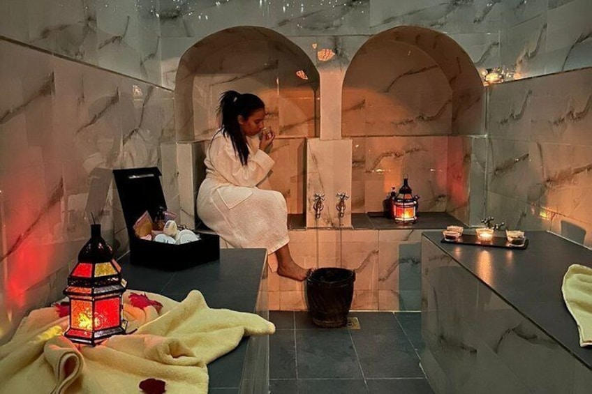 A person in a robe in a spa-like setting with marble walls, a lantern, and candles. 4