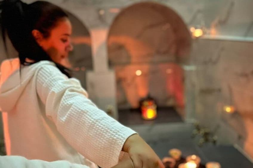 A person in a white robe reaching towards a lit candle on a table. 3