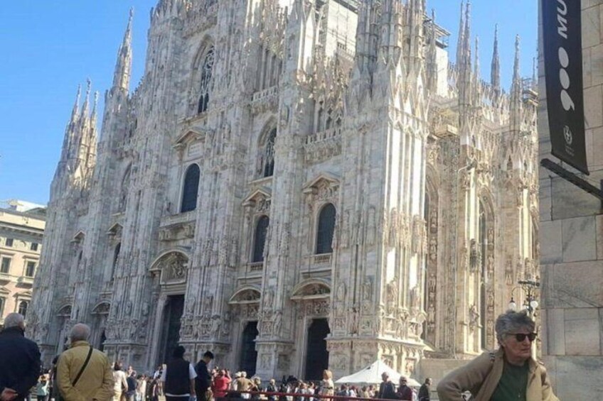 A historic cathedral with intricate Gothic architecture, a crowd of people, and a clear blue sky. 1