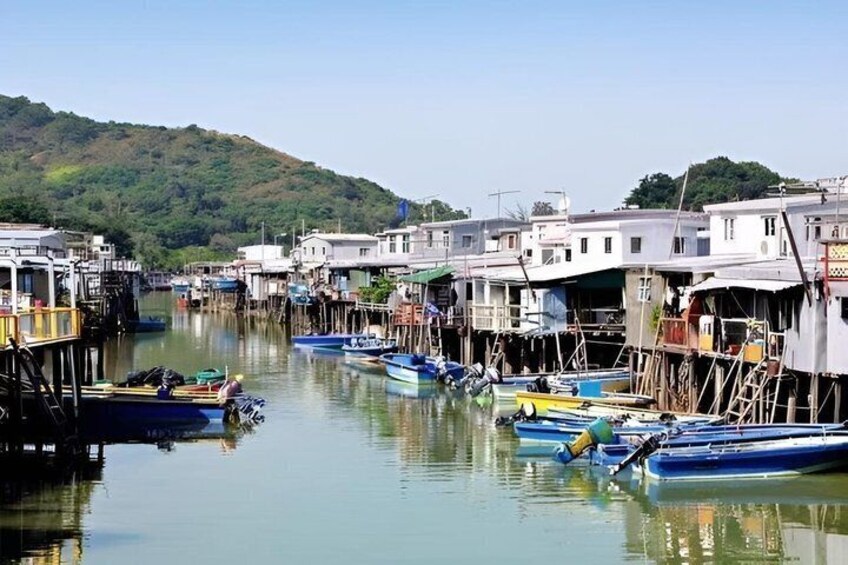 A calm waterway with boats docked along the shore, surrounded by residential buildings and a hill in the background. 5