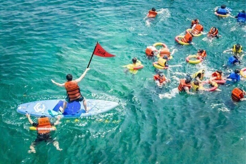Eine Gruppe von Menschen im Wasser mit Schwimmwesten und eine Person auf einem Paddleboard, die eine Flagge hält. 4