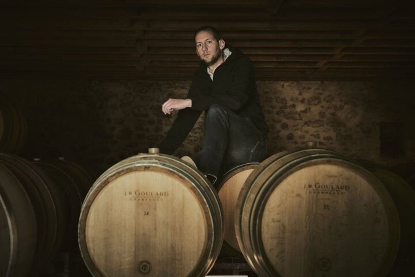 A person sitting on a barrel in a cellar with wooden walls and barrels. 3