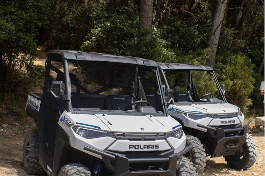 Two Polaris off-road vehicles parked on a dirt path surrounded by trees. 3