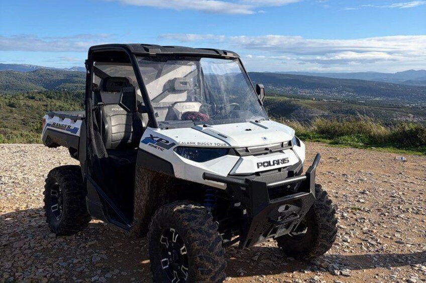 A white Polaris X2 RANGER 4x4 vehicle parked on a gravel path with a scenic view of mountains and a clear sky in the background. 2