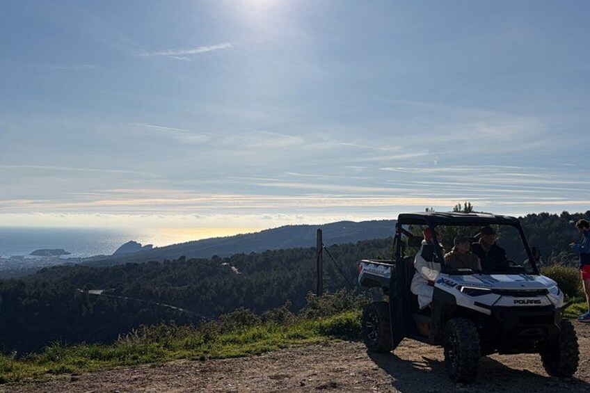 A Polaris off-road vehicle on a dirt path with a scenic view of a forested landscape and a body of water in the distance. 5