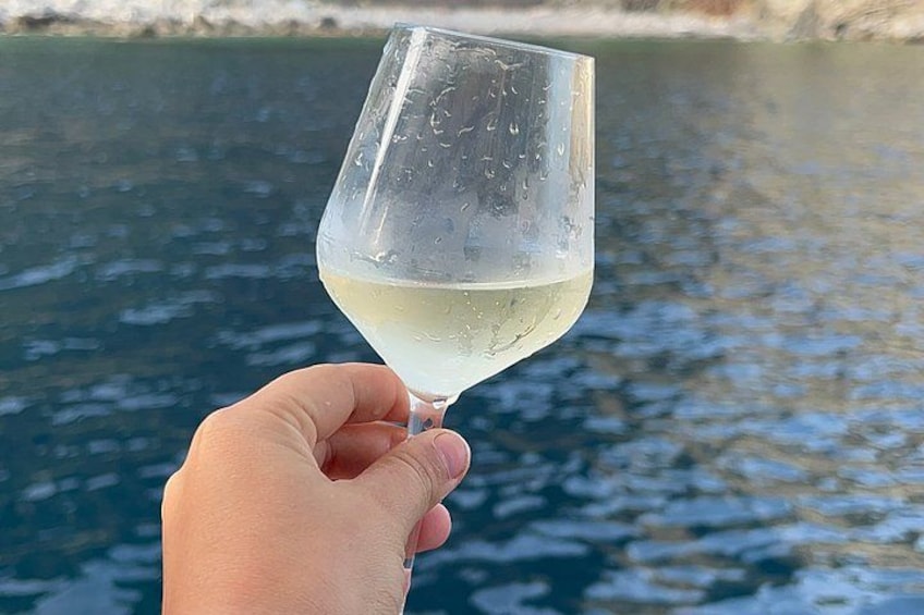 Eine Hand hält ein Glas Weißwein vor einer Wasserfläche. 2