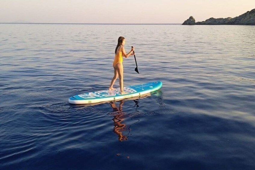 A person paddleboarding on calm water with a clear sky and distant land. 4