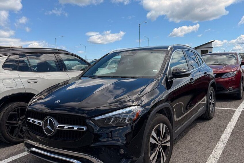 A black SUV parked in a lot with other vehicles, clear skies, and a building in the background. 3