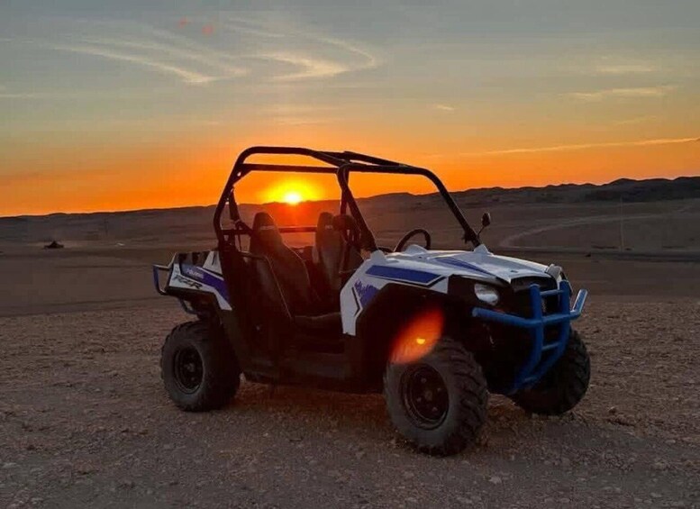 A white and blue off-road vehicle parked on a dirt surface with a sunset in the background. 5