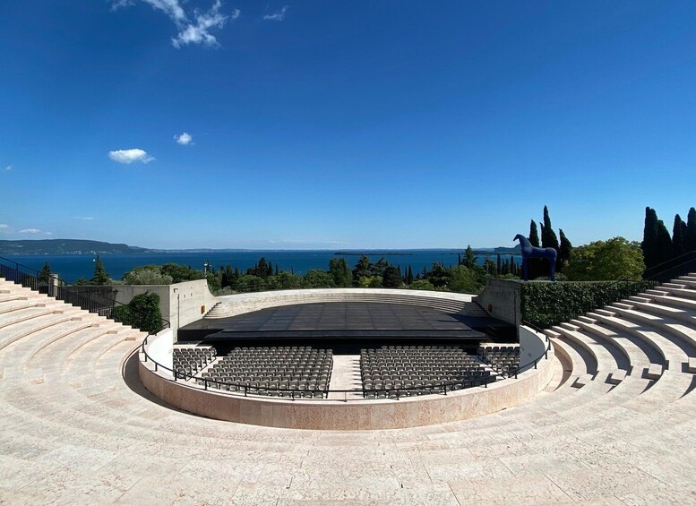 An outdoor amphitheater with tiered seating and a stage, overlooking a coastal landscape. 3