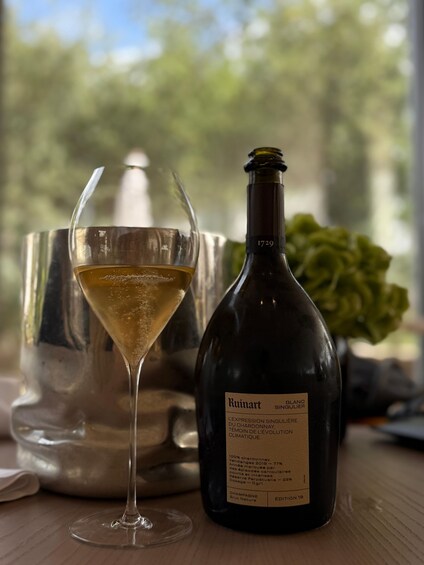 A bottle of Ruimitart Blanc Singulier wine and a glass of white wine on a wooden table with a blurred outdoor background. 5