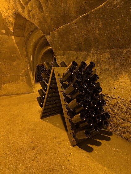 A wine rack with bottles in a dimly lit room with rough walls. 2