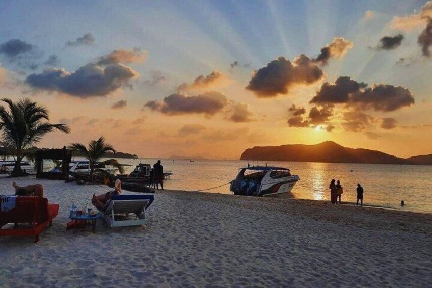 Una spiaggia con lettini, una barca e un tramonto sull'acqua. 1