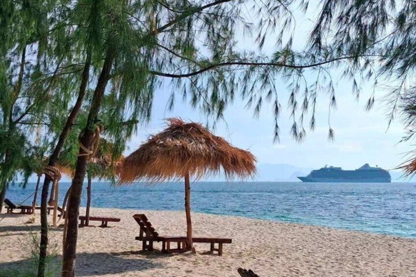 Una spiaggia con ombrelloni di paglia, sedie di legno e un mare calmo con un'isola all'orizzonte. 4