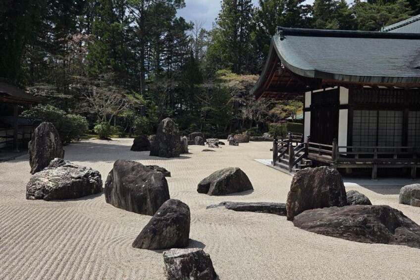 A traditional Japanese garden with large rocks, a wooden building, and a wooden bridge. 3