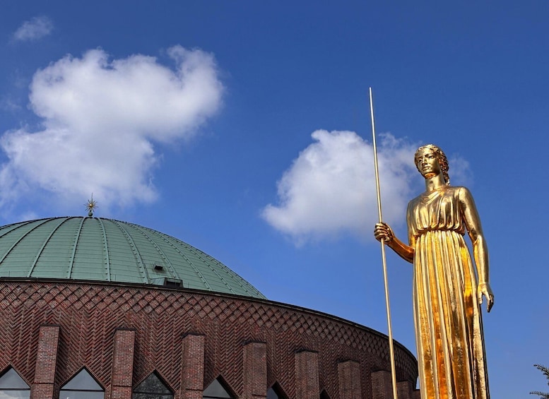 A golden statue of a figure holding a spear, a green dome, and a brick building with triangular windows. 2