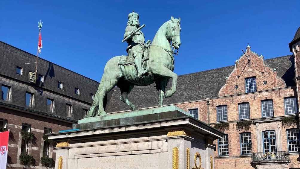 A statue of a man on horseback in front of a historic building with a flag. 1