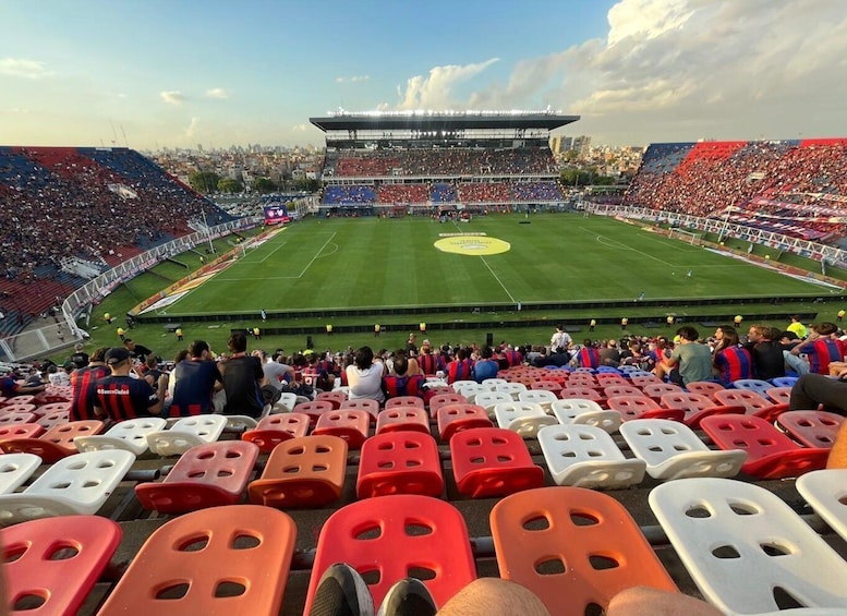A stadium with a football pitch, spectators, and a cityscape in the background. 1