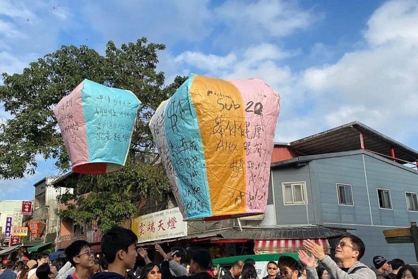 A crowd of people holding colorful paper lanterns with writing on them. 2