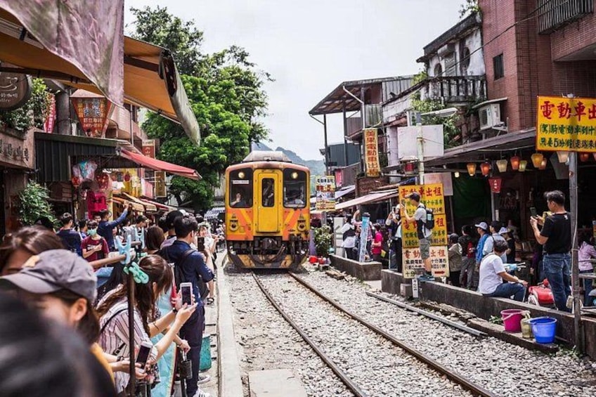 A train passing through a crowded street with people standing and sitting on the sides. 3