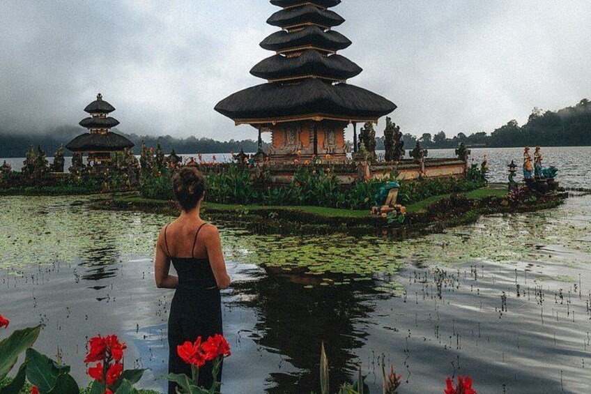 Una mujer con un vestido negro está de pie junto a un estanque con una pagoda y flores de loto. 4