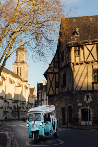 A vintage blue van with a white roof driving on a cobblestone street in a historic town with medieval architecture. 3