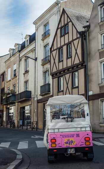 A pink tuk-tuk parked on a street with a half-timbered building in the background. 5