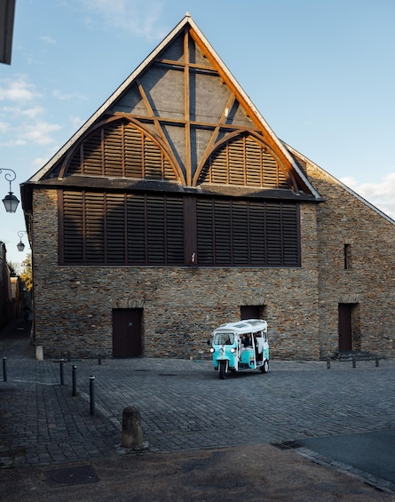 A stone building with a wooden gable roof and a vintage blue vehicle parked in front. 4