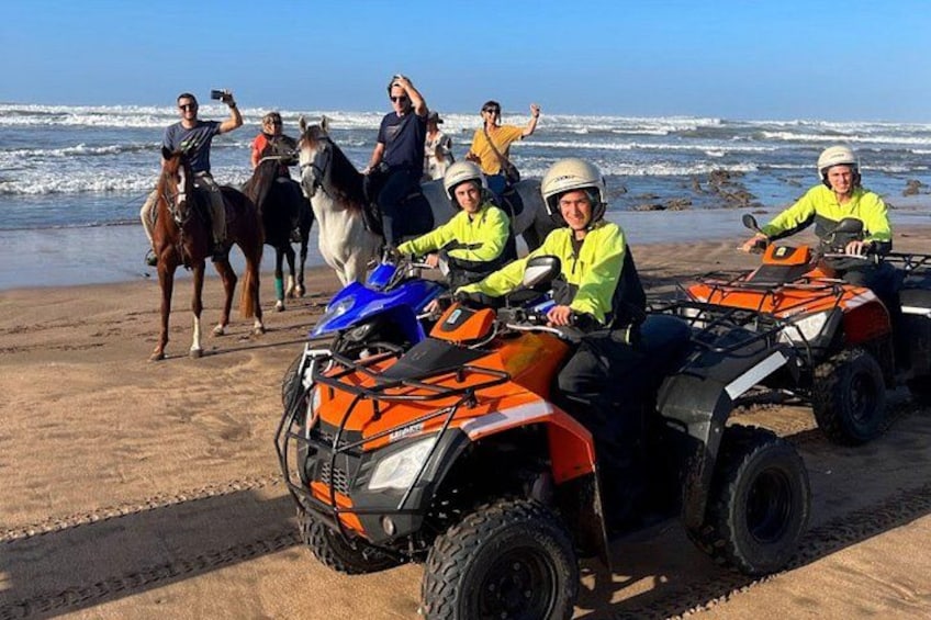 People riding ATVs on a beach with horses in the background. 2