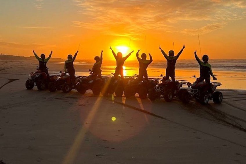 A group of people on ATVs on a beach at sunset. 1