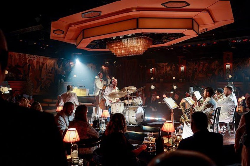 A jazz band performing on a stage with a chandelier and audience seated at tables. 4