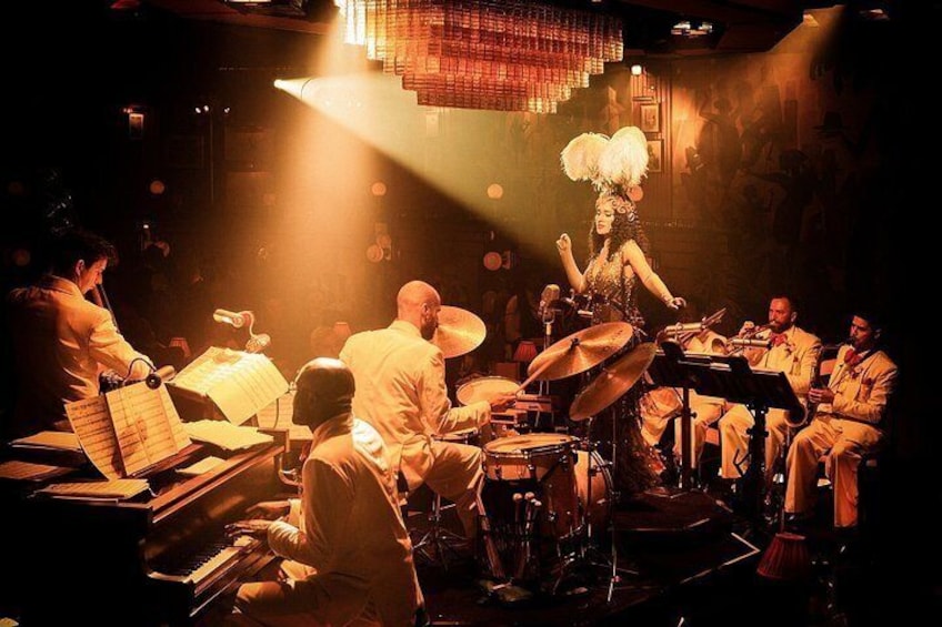 A jazz band performing on stage with musicians seated around a piano and drums. 4
