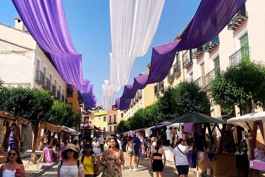 A street lined with buildings, draped with purple and white fabric. 3