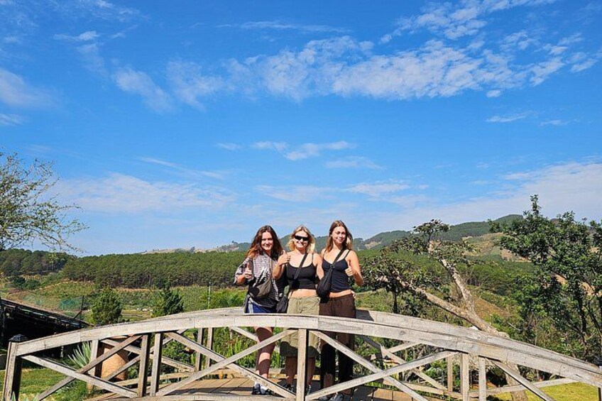 Tres personas de pie sobre un puente de madera, con un paisaje montañoso al fondo. 5