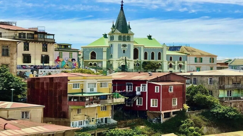 A church with a green roof and a tall spire, surrounded by colorful buildings. 1