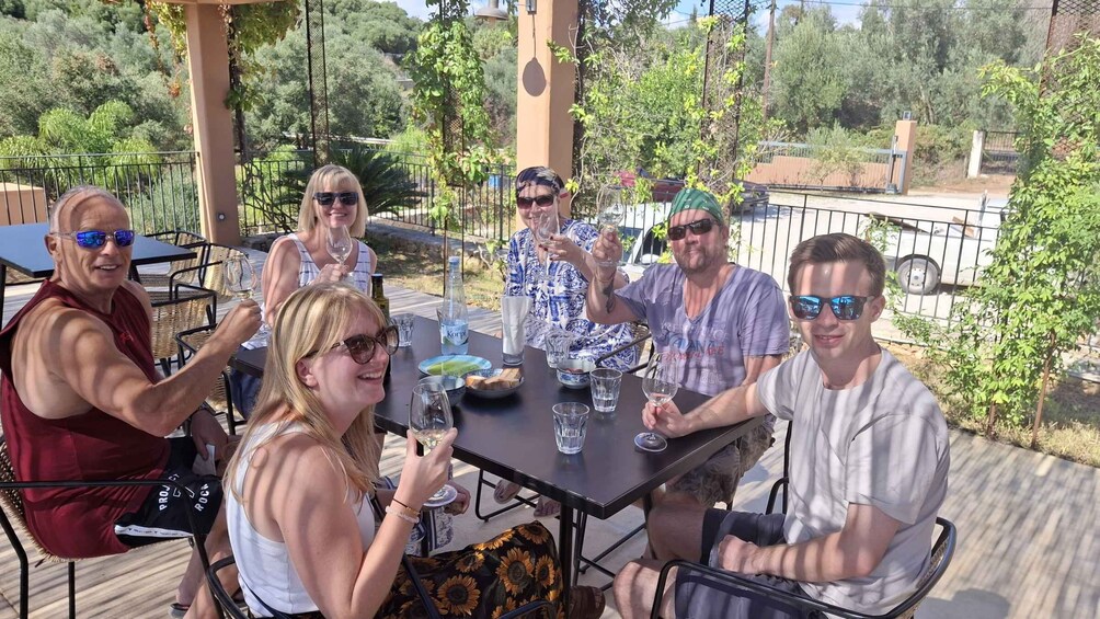 A group of people sitting at an outdoor table with drinks, surrounded by greenery and a fence. 5